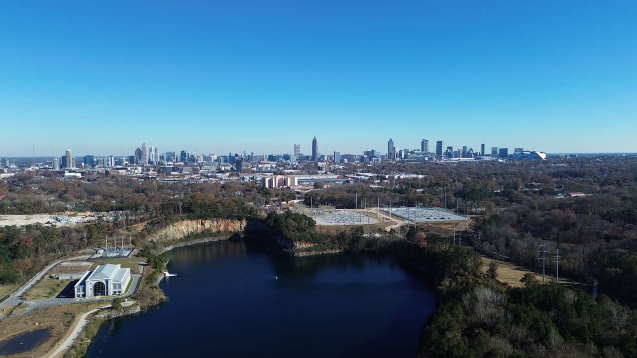 Aerial view of Bolton area in GA showing a blue reservoir with rock quarry walls, surrounding trees, and the Atlanta skyline.