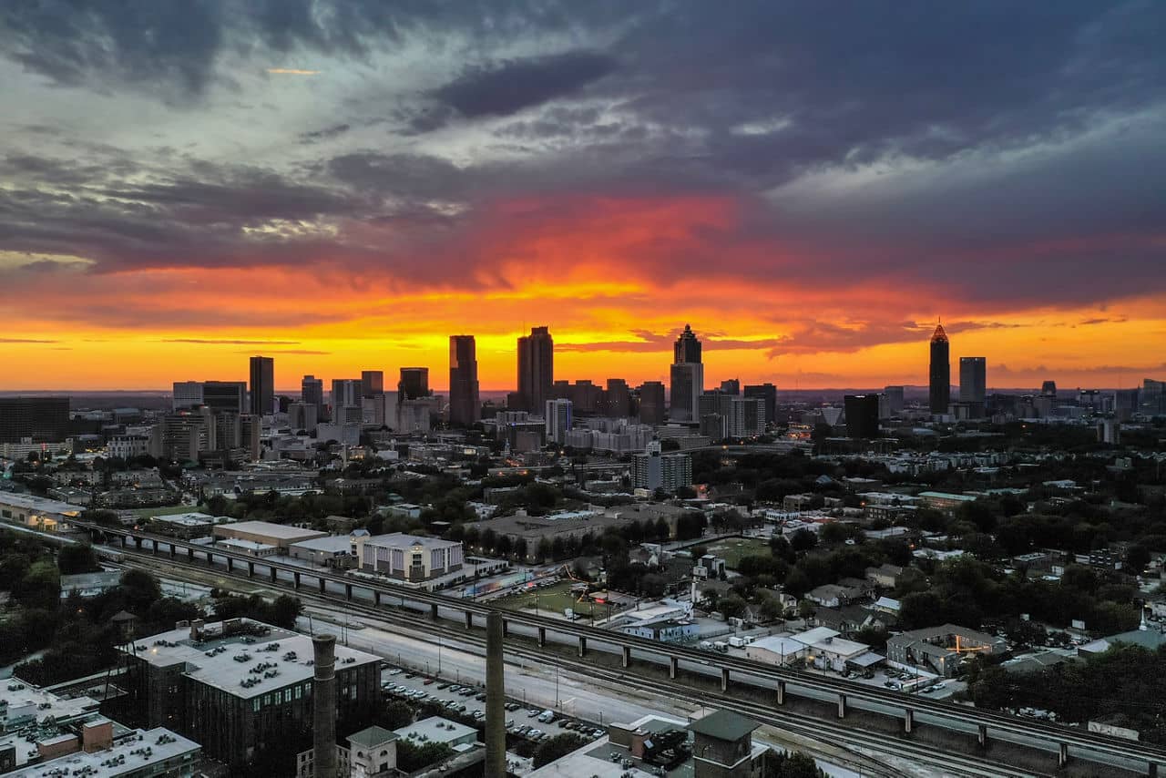 Dramatic sunset over Atlanta skyline viewed from Grant Park, GA with orange-red sky, silhouetted skyscrapers, and transit lines below.