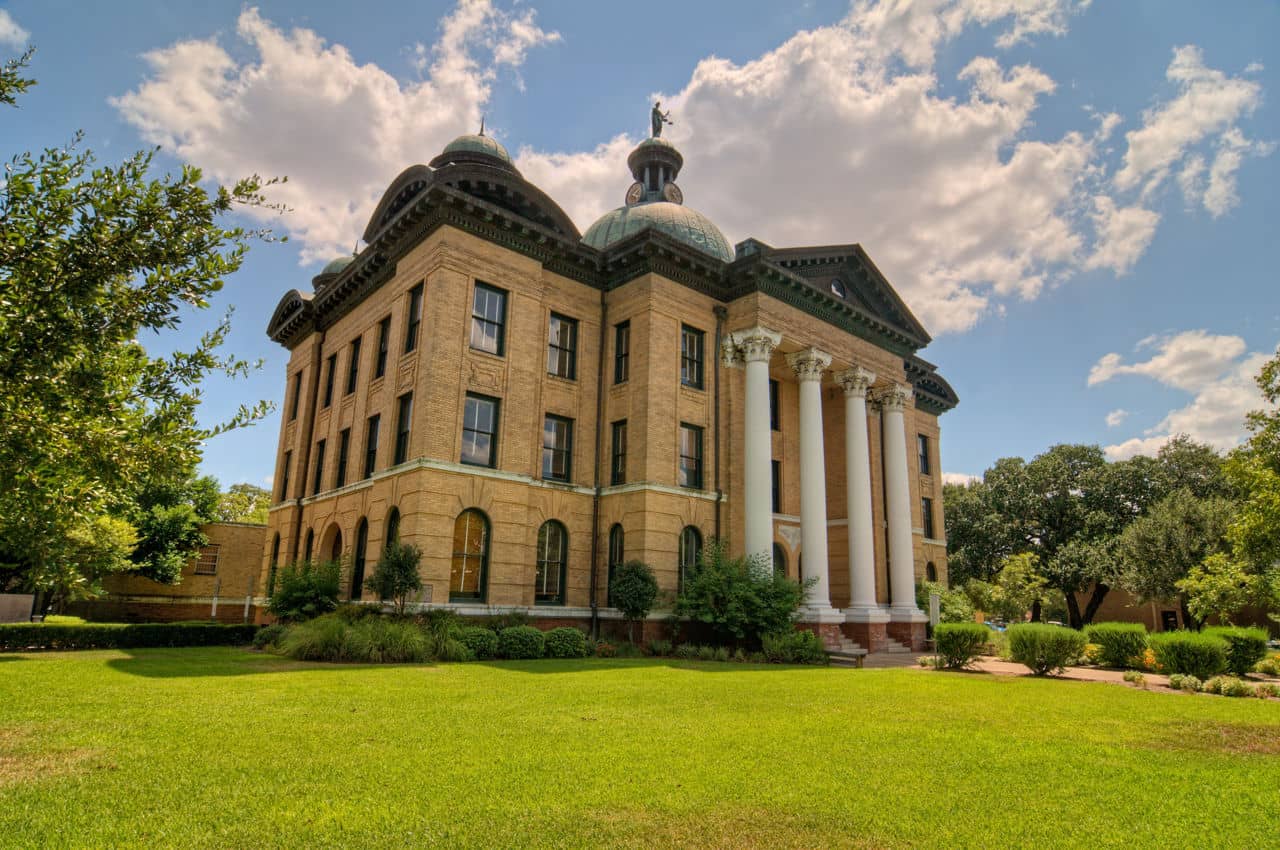 Historic building in Richmond, Texas, featuring large pillars, a dome, and surrounded by green grass and trees.